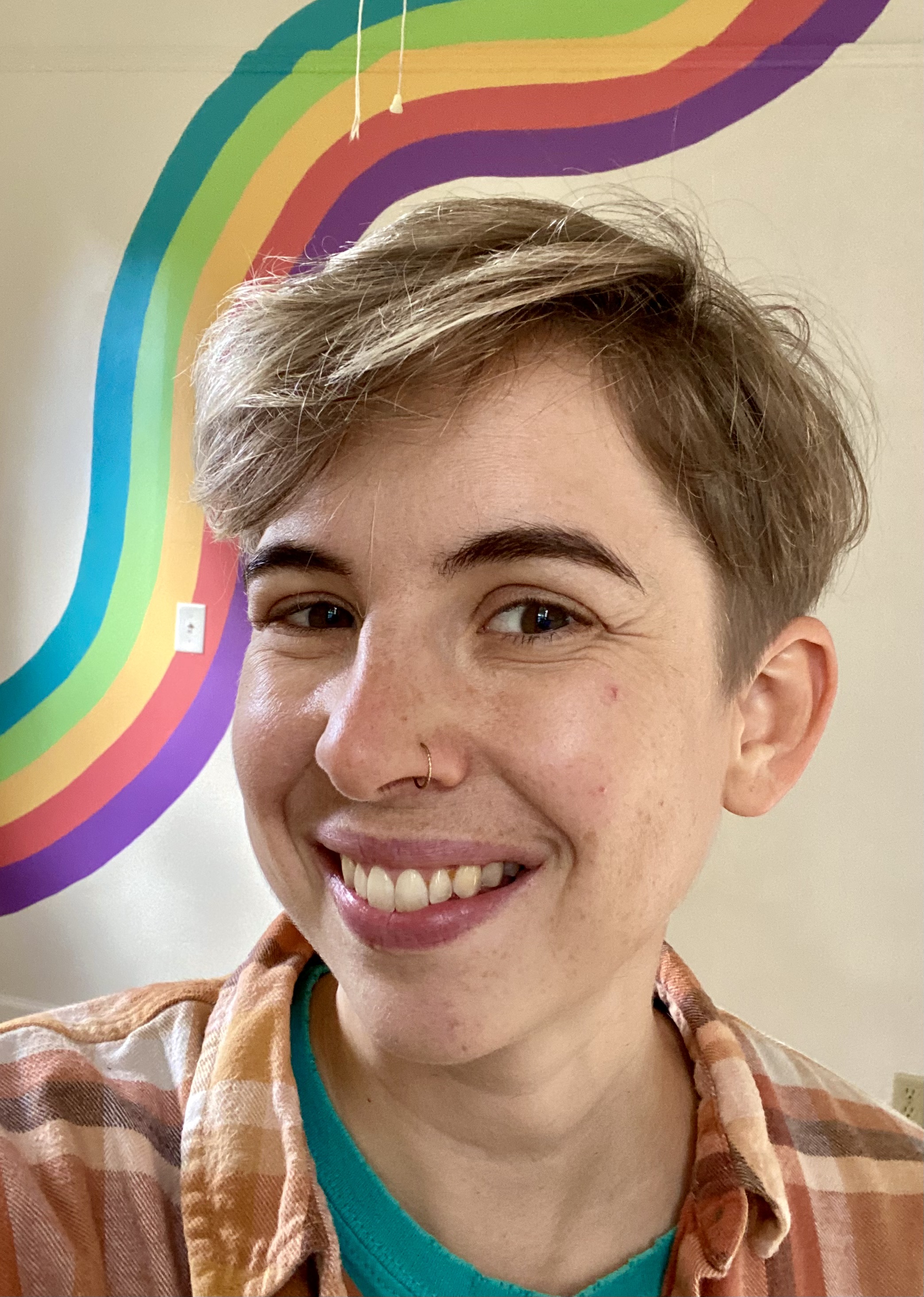 Mel smiling with a rainbow background